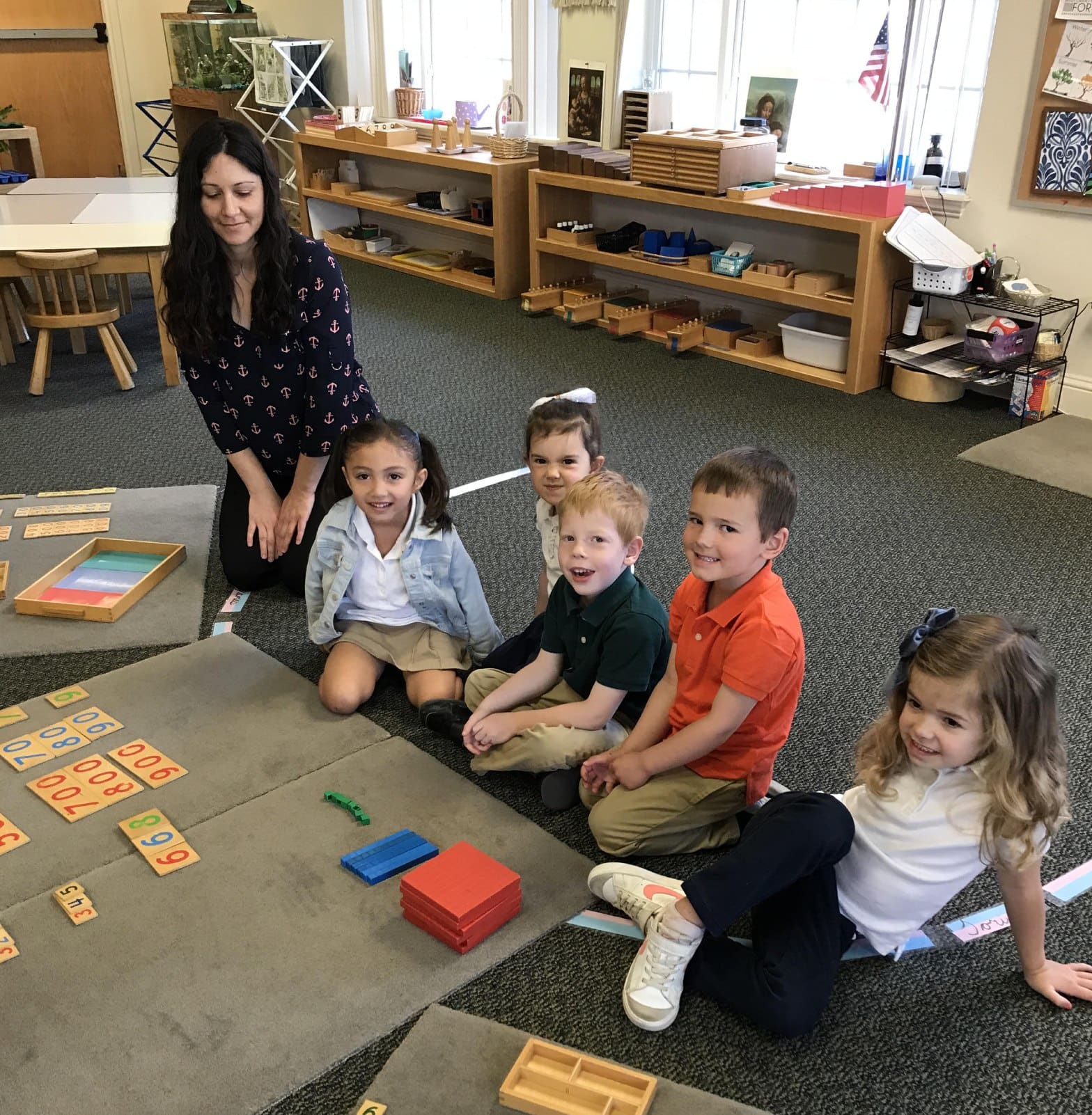 A group of children sitting on the floor in front of a teacher.