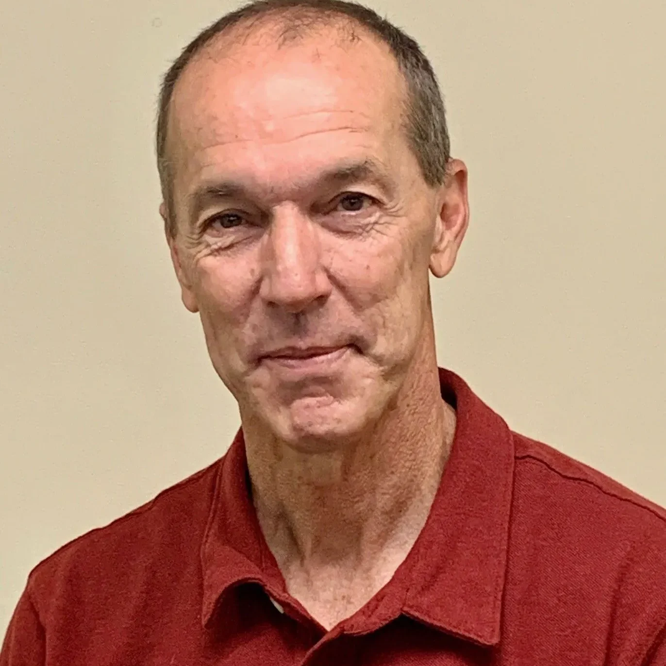 A man in red shirt standing next to wall.