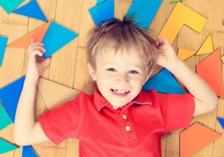 A young boy laying on the floor with many colorful shapes.